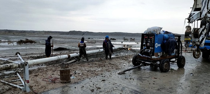 中国石油管道局焊接机组工人在抢修现场，趁暴雨间歇在泥地中进行组对焊接。中国石油管道局供图